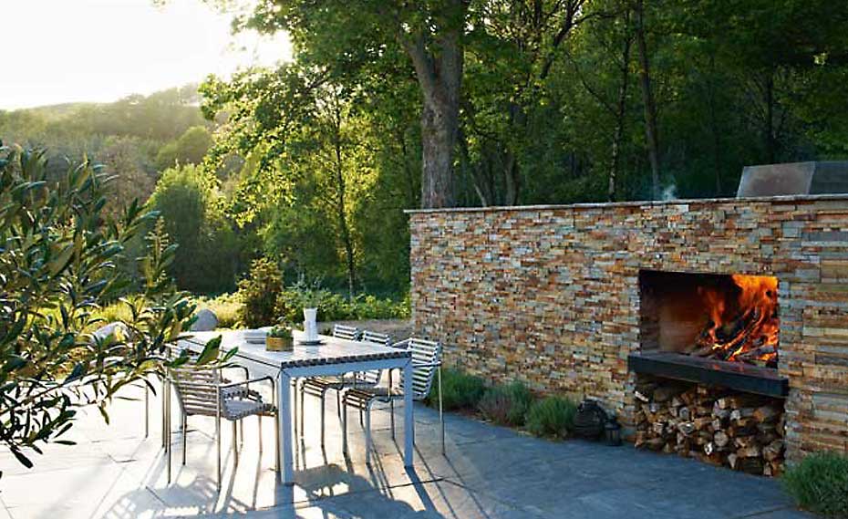 Outdoor Stone Veneer Fireplace with Norstone Ochre Blend Stacked Stone Rock Panels In a Garden