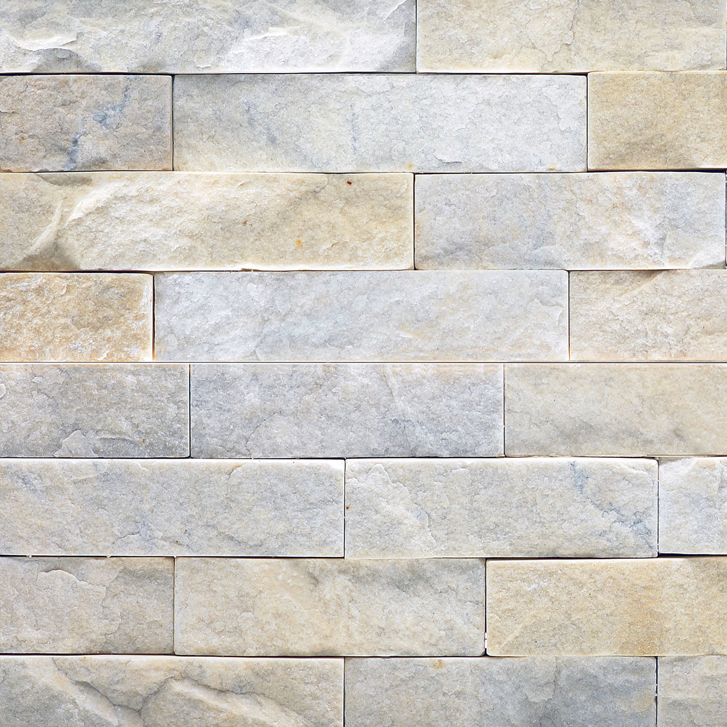 A close-up view of a light-colored stone veneer wall with rectangular tiles arranged in a staggered pattern. The surface texture is rough and natural, displaying subtle variations in shade and color.