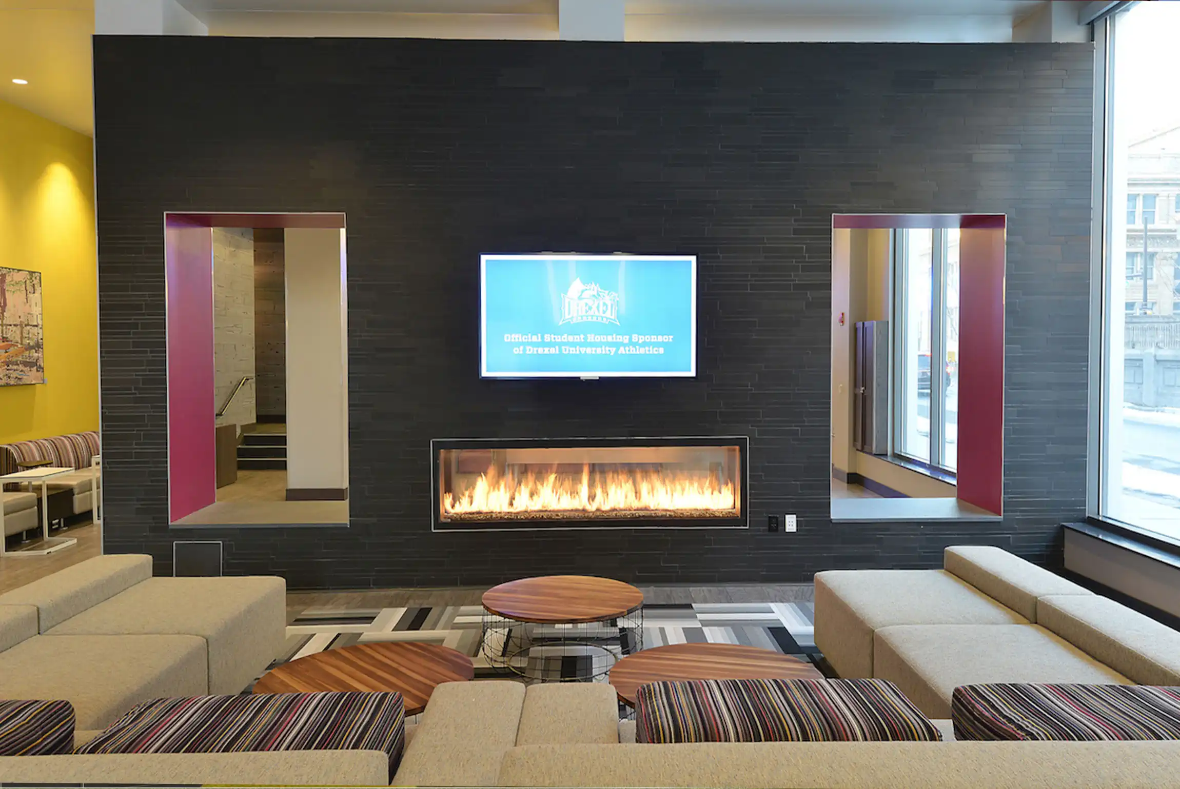 Norstone Ebony Basalt Lynia tiles on a large feature wall in the common space of a multi family building with a tv and linear gas fireplace