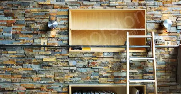A wooden ladder leans against a high end stone design accent wall with built-in wooden shelves, two wall-mounted circular lights, and a level tool resting on one of the shelves.