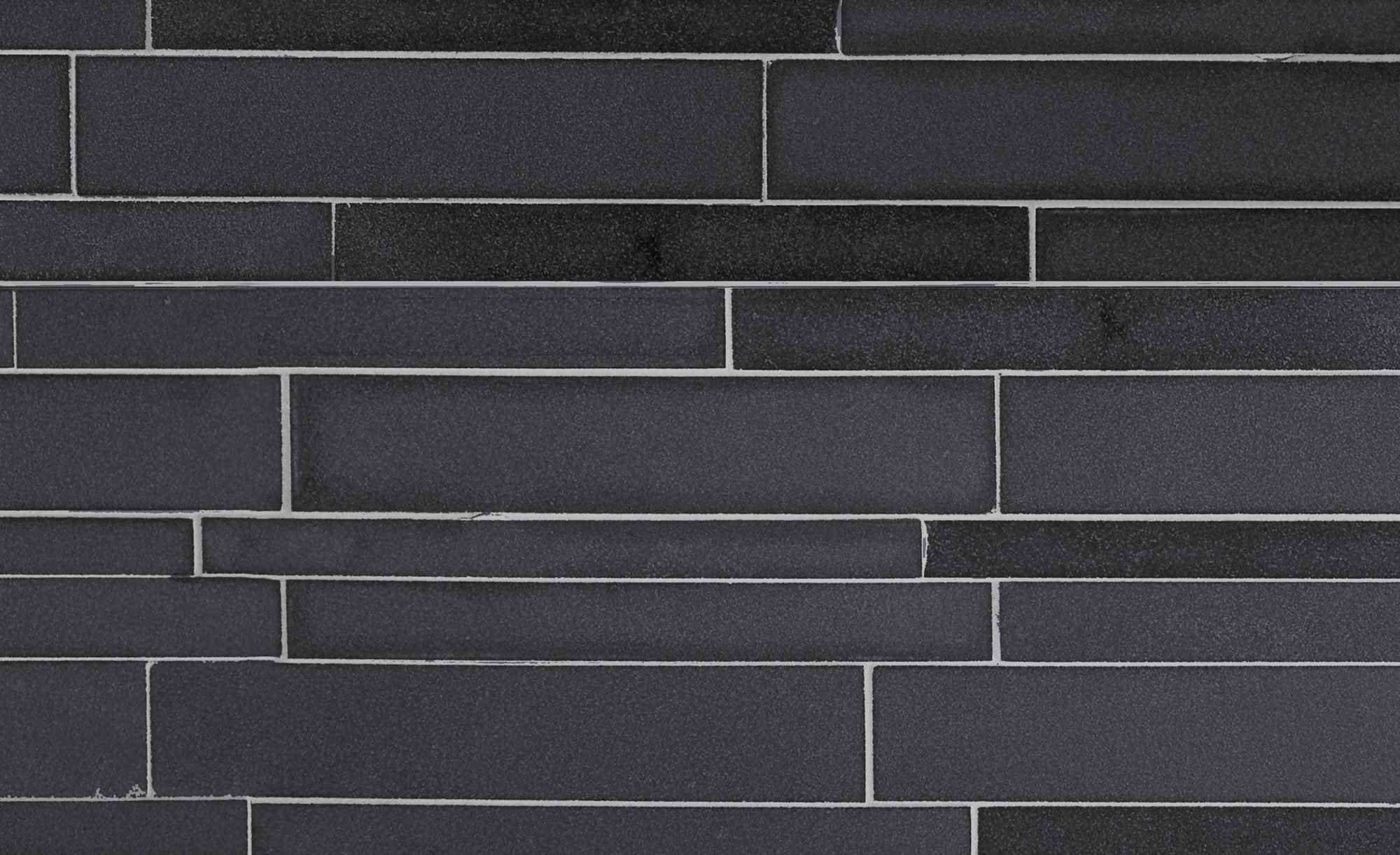 A close-up view of a dark gray brick wall with rectangular bricks arranged in a horizontal pattern and light-colored mortar lines, showcasing the refined texture of a high end stone design.