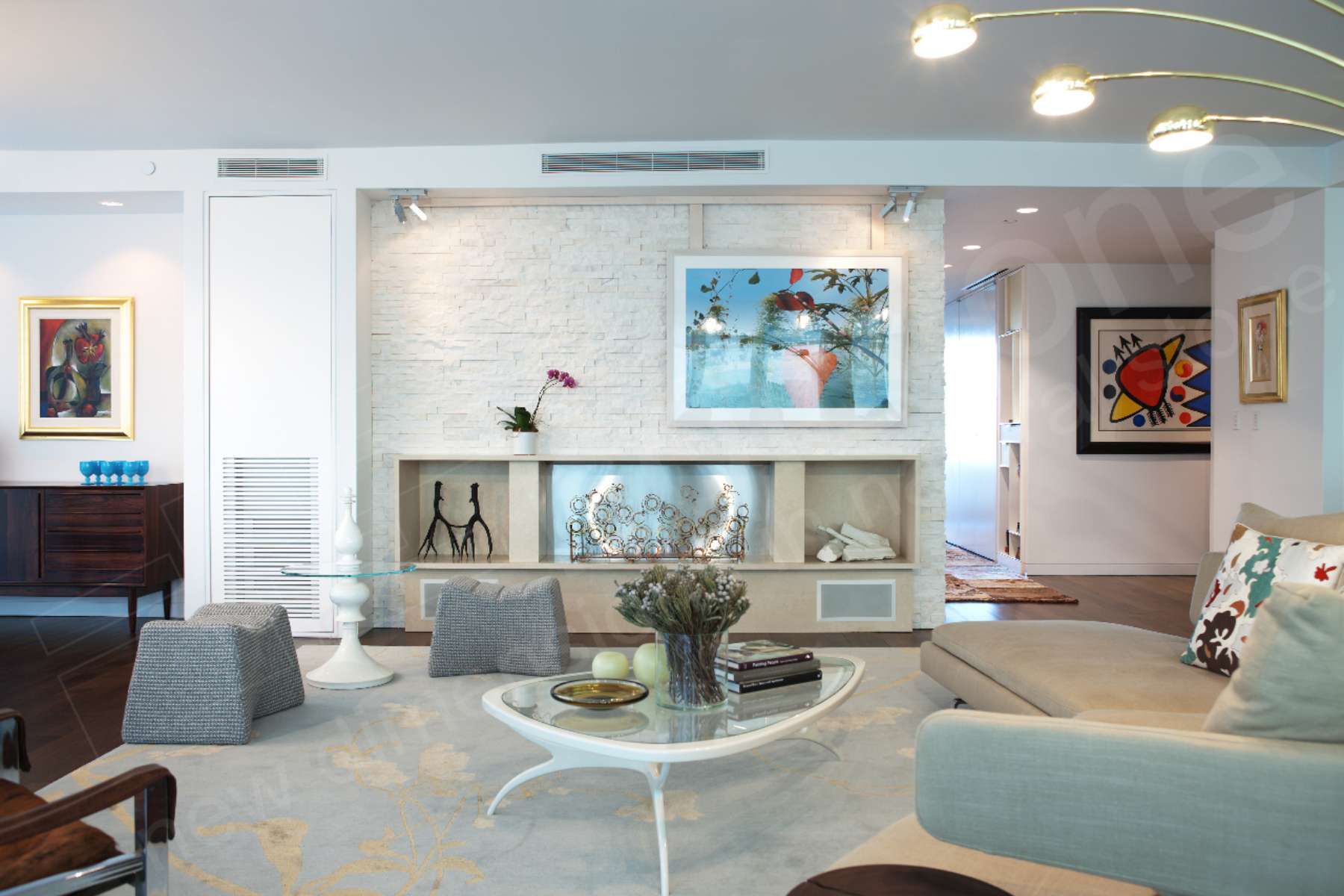 Modern living room with a light color palette, abstract art, a cream sectional sofa, a glass coffee table, decorative accents, cube ottomans, built-in shelves, and a stone accent wall featuring a large framed photo.