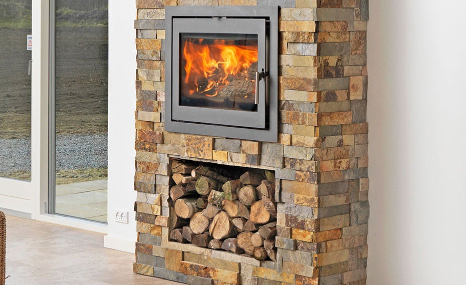 stacked stone wall behind wood stove with firewood storage and natural stone veneer surround